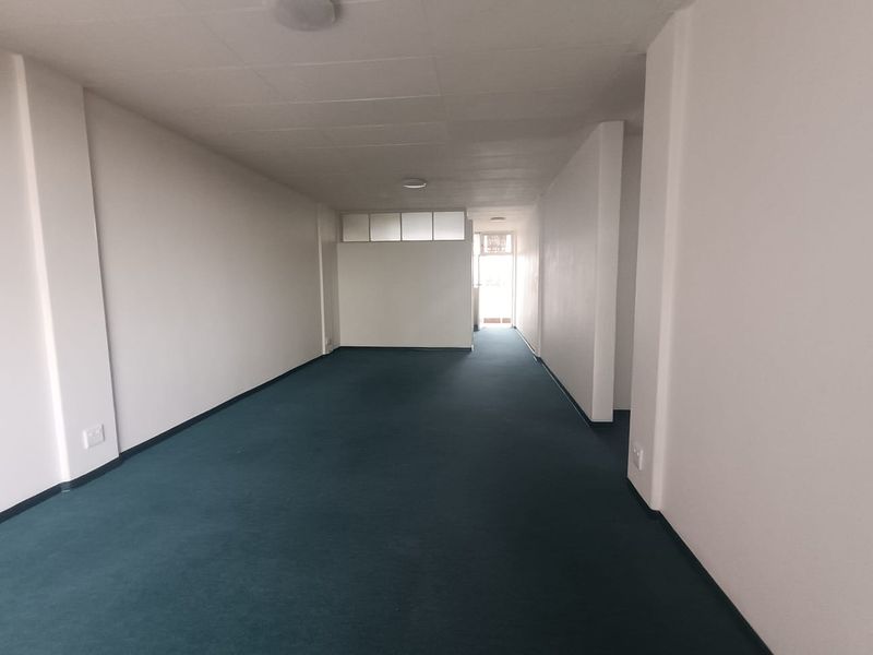 A spacious, empty living area featuring neutral walls, carpeted flooring, and natural light from the rear entrance.