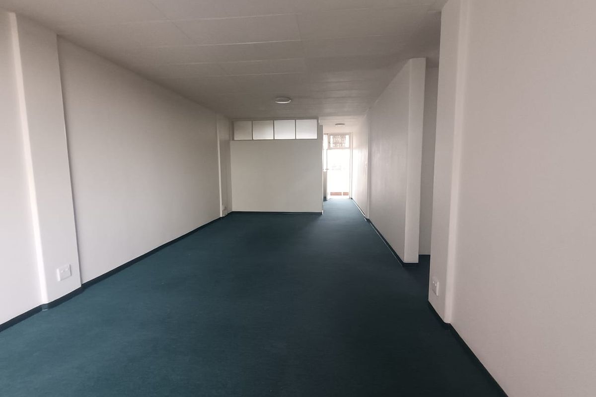 A spacious, empty living area featuring neutral walls, carpeted flooring, and natural light from the rear entrance.