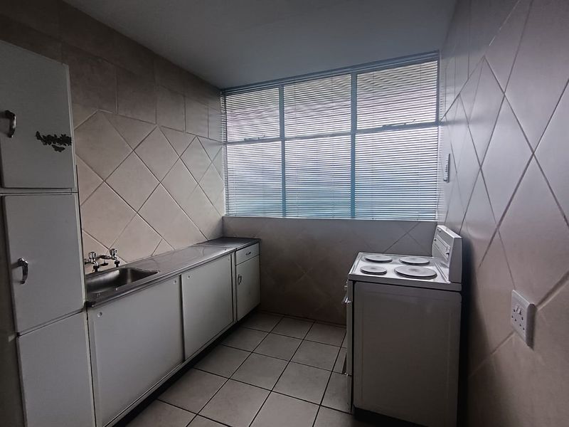 A functional kitchen featuring tiled walls, built-in cabinetry, a stainless steel sink, and an electric stove, offering a practical layout with natural light.