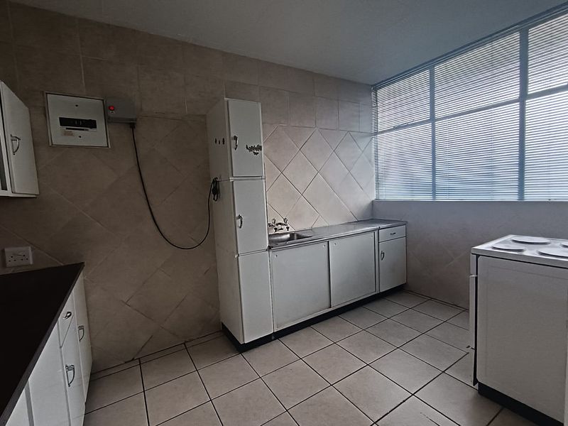 A functional kitchen featuring tiled walls and flooring, built-in cabinetry with a stainless steel sink, and large windows providing ample natural light.