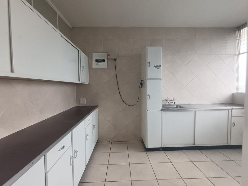A functional, empty kitchen featuring built-in white cabinetry, a stainless steel sink, and tiled finishes, offering a blank canvas for modern renovation.
