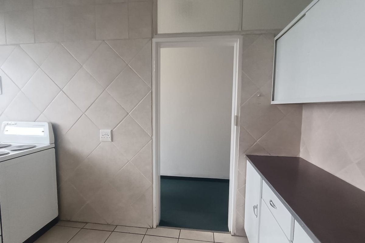 A functional kitchen featuring tiled walls and flooring, built-in cabinetry with laminate countertops, and a freestanding stove, with a doorway leading to an adjacent room.