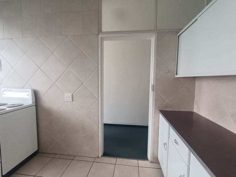 A functional kitchen featuring tiled walls and flooring, built-in cabinetry with laminate countertops, and a freestanding stove, with a doorway leading to an adjacent room.