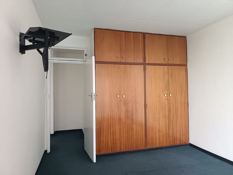 A bedroom featuring built-in wooden cupboards, a wall-mounted television bracket, and carpeted flooring.