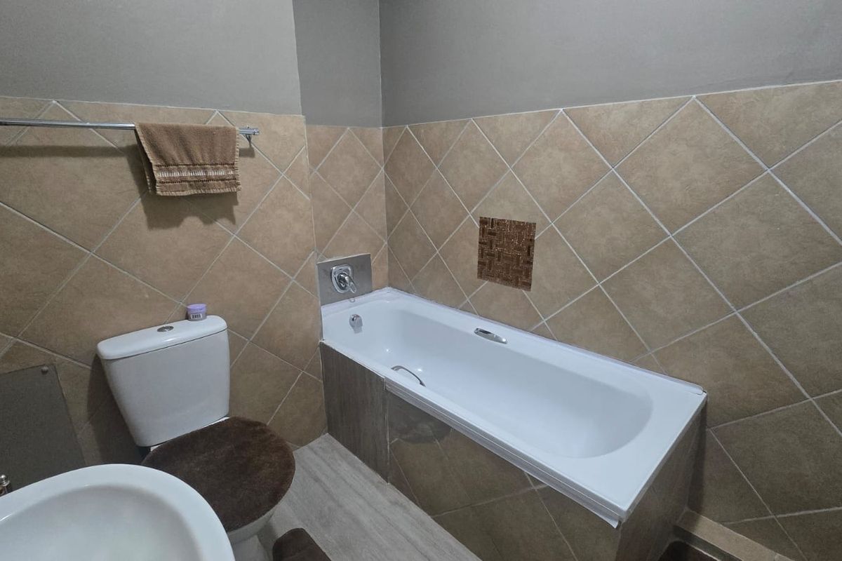 A functional bathroom featuring a standard bathtub, toilet, and basin with neutral-toned wall tiling and a towel rail.