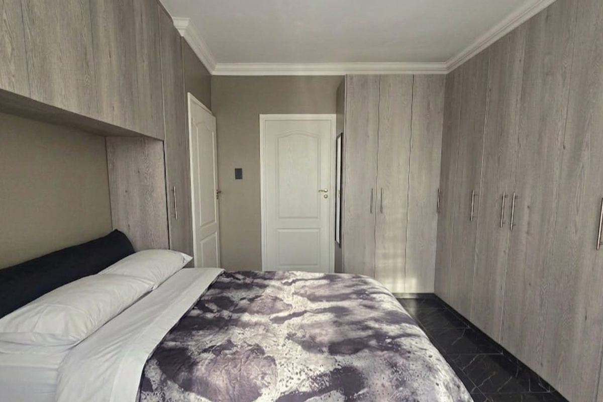 A well-maintained bedroom featuring extensive built-in cabinetry with a modern wood-grain finish, crown molding, and dark tiled flooring.