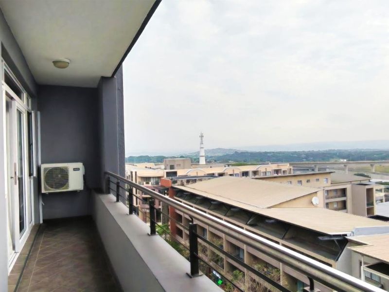 A spacious covered balcony featuring tiled flooring, a metal balustrade, and expansive views of the surrounding neighborhood and infrastructure.