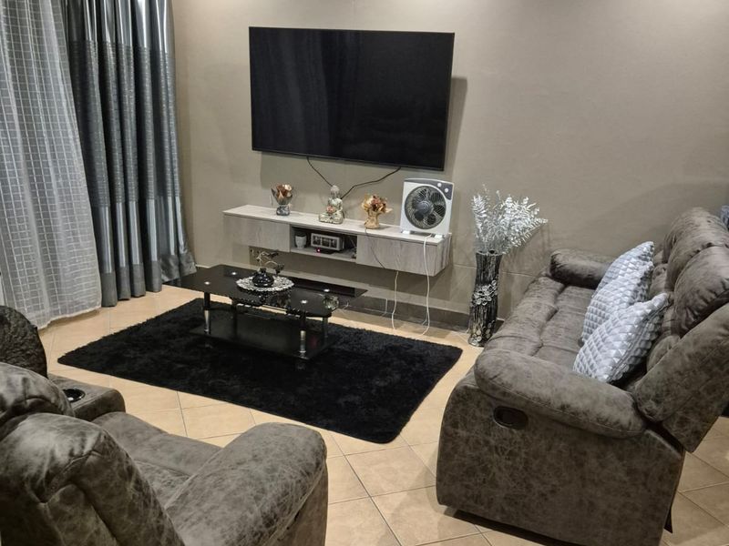 A comfortable living room featuring ceramic floor tiles, recessed downlighting, and a wall-mounted floating media console.