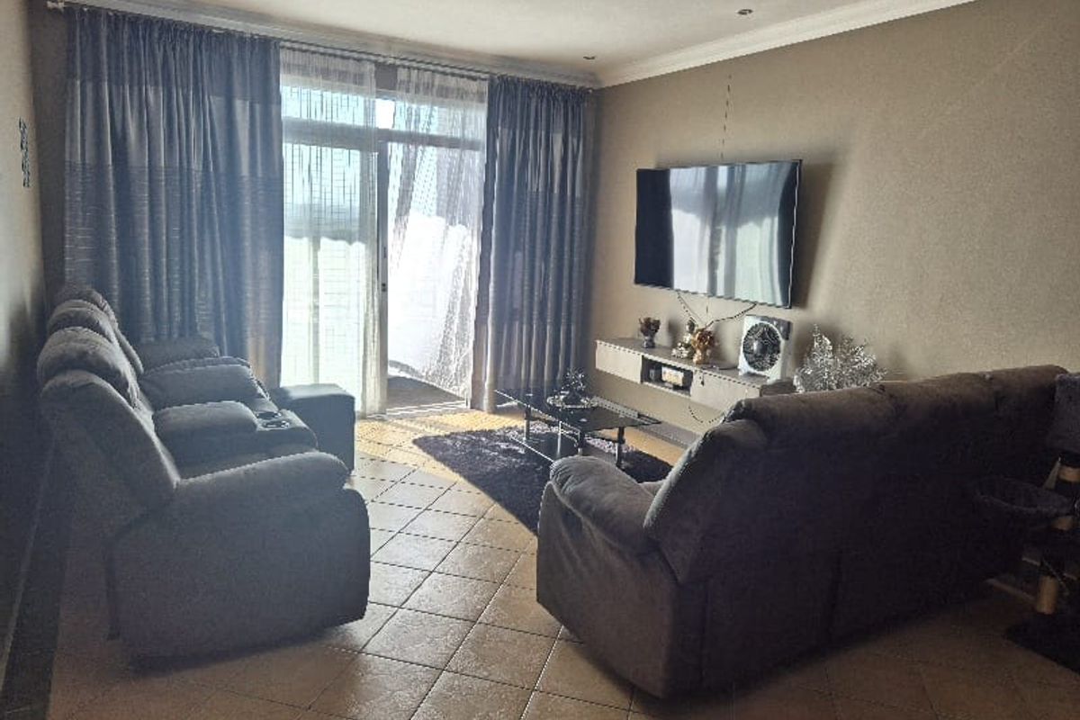 A comfortable living room featuring tiled flooring, a floating media console, and a large sliding glass door providing access to the balcony.