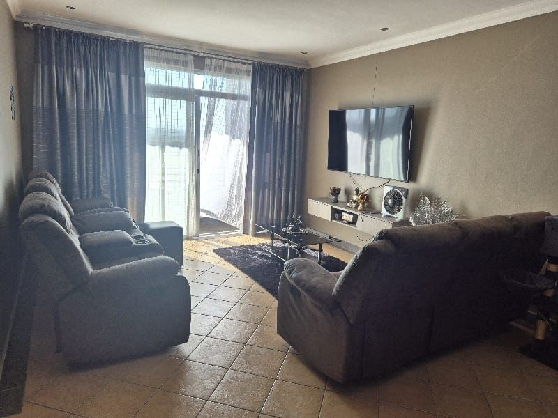 A comfortable living room featuring tiled flooring, a floating media console, and a large sliding glass door providing access to the balcony.