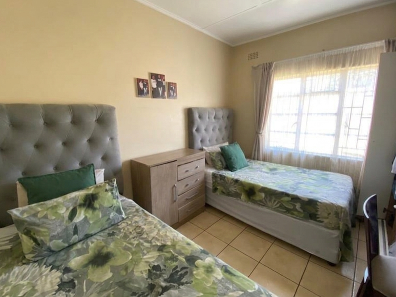 A functional bedroom featuring tiled flooring, a large window with security bars, and a built-in wardrobe, offering a comfortable living space.