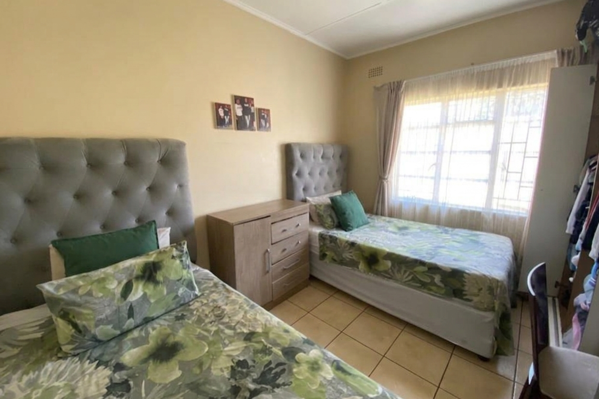 A functional bedroom featuring tiled flooring, a large window with security bars, and a built-in wardrobe, offering a comfortable living space.