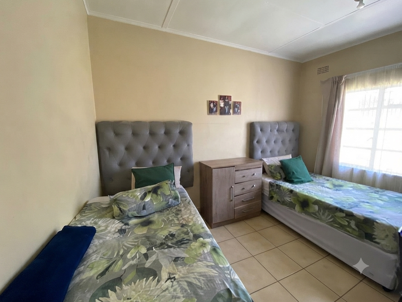 A functional bedroom featuring tiled flooring and a window fitted with security bars, providing natural light and ventilation.