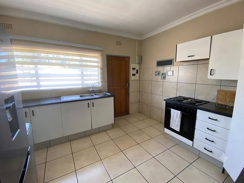 A functional kitchen featuring white cabinetry, tiled backsplash, tiled flooring, and a freestanding stove with a window providing natural light.