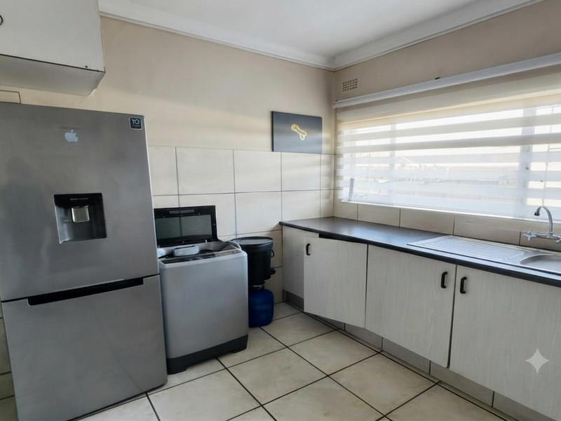 A functional kitchen area featuring built-in cabinetry, tiled backsplash, and a stainless steel sink with natural light from a large window.