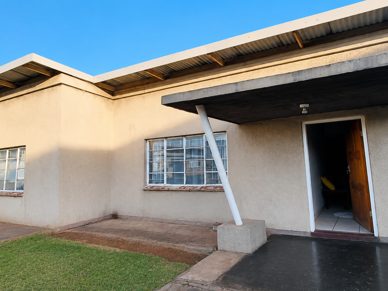 Front exterior view of the apartment featuring a covered patio, steel-framed windows, and a wooden entrance door under a corrugated metal roof.