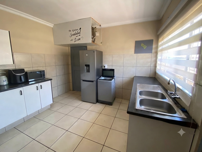 Functional kitchen featuring tiled splashbacks, double bowl sink, and ample cabinetry, offering a practical layout with potential for cosmetic updates.