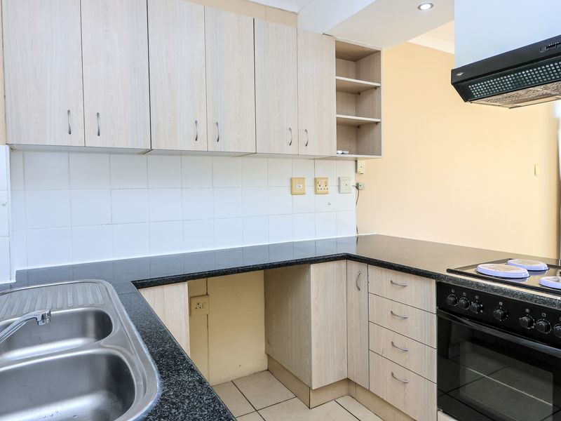 A functional kitchen featuring light wood-tone cabinetry, dark laminate countertops, a double stainless steel sink, and integrated oven with extractor fan.