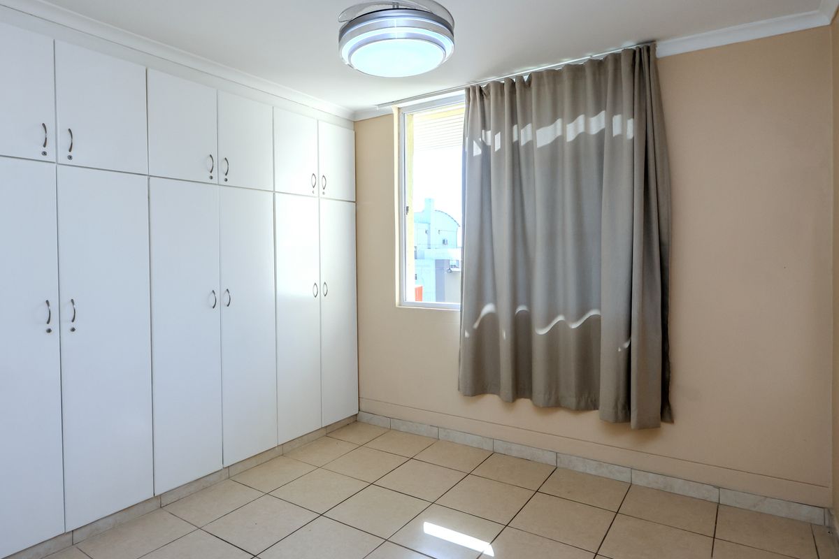 A clean, empty bedroom featuring neutral tiled flooring, ample built-in cupboard storage, and a window providing natural light.