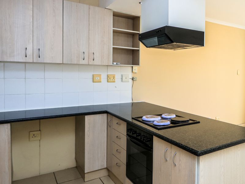 A functional kitchen featuring light wood-look cabinetry, dark granite countertops, a built-in oven with hob, and an extractor fan.