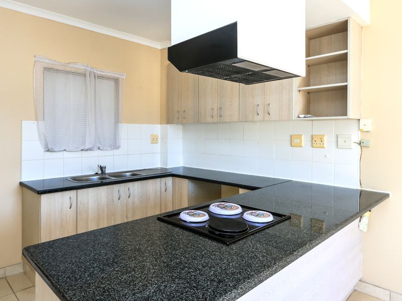 A functional kitchen featuring granite countertops, built-in cabinetry, an electric hob, and an extractor fan, offering a clean space ready for updates.