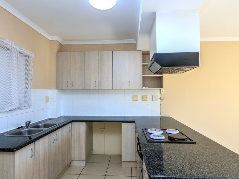Functional kitchen featuring laminate cabinetry, granite countertops, a built-in hob with extractor fan, and tiled splashbacks in a neutral color palette.