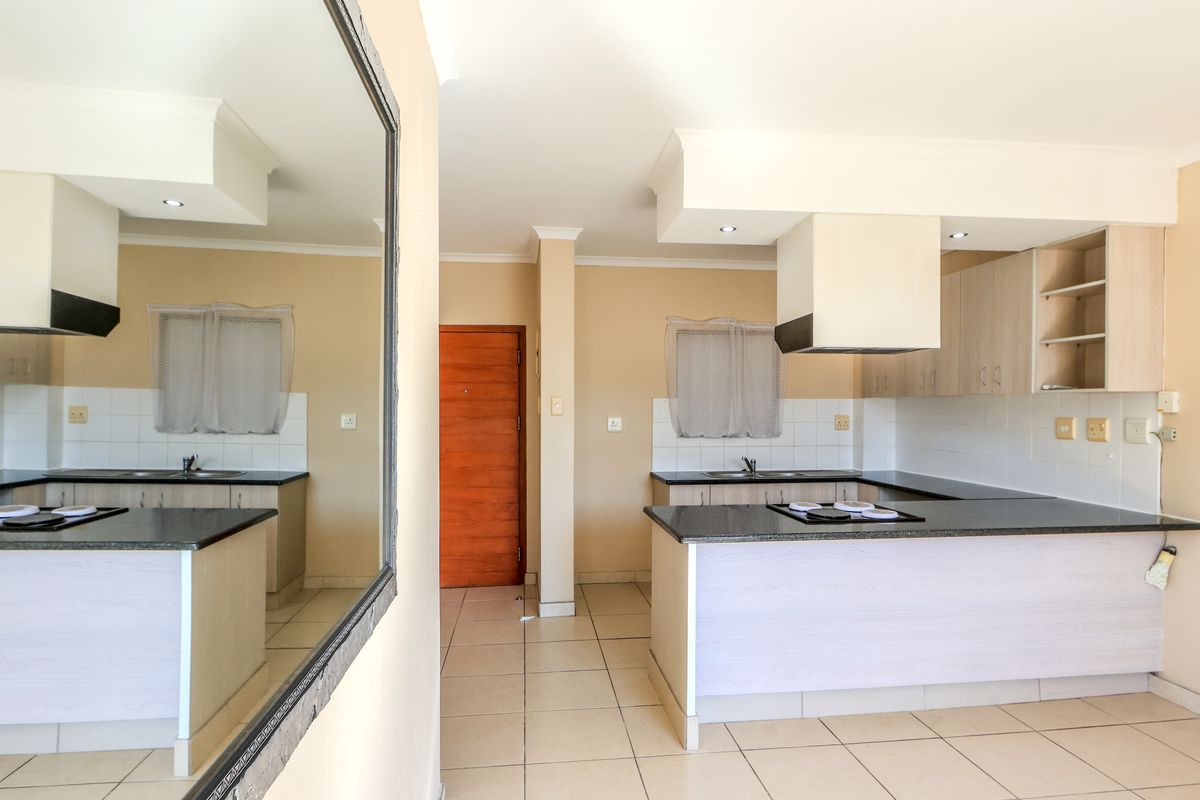 A functional kitchen featuring built-in cabinetry, granite countertops, a hob with an extractor fan, and tiled flooring in an open-plan layout.