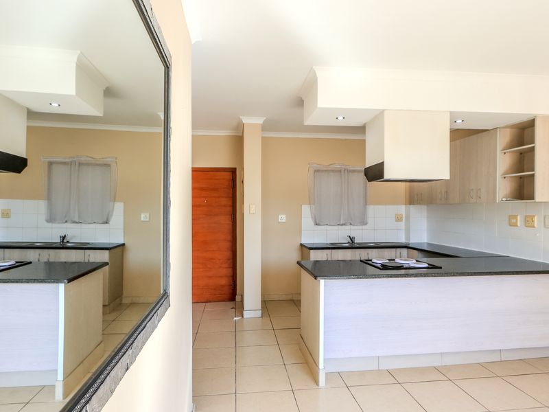 A functional kitchen featuring built-in cabinetry, granite countertops, a hob with an extractor fan, and tiled flooring in an open-plan layout.