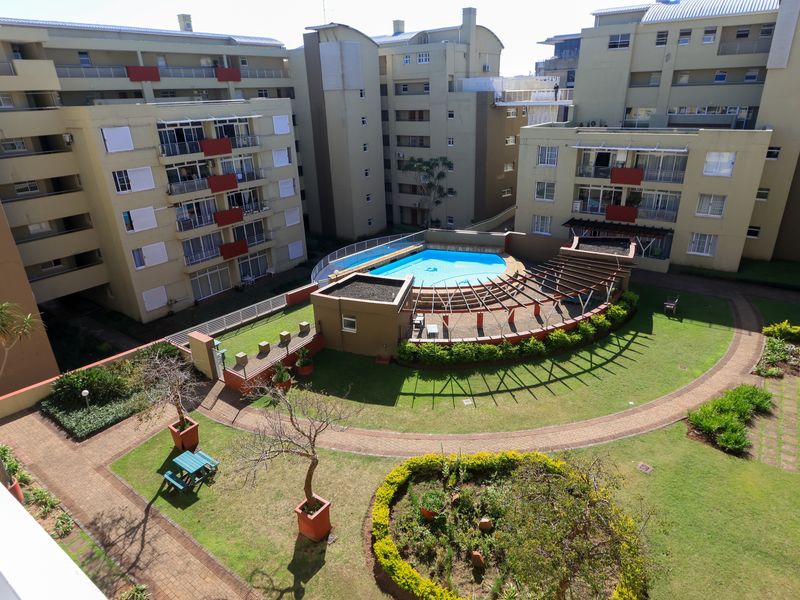 Aerial view of an apartment complex courtyard featuring a central swimming pool, landscaped gardens, paved pathways, and a pergola structure.