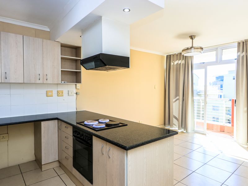 Open-plan kitchen and living area featuring light wood cabinetry, granite countertops, built-in appliances, and direct access to a balcony through sliding glass doors.