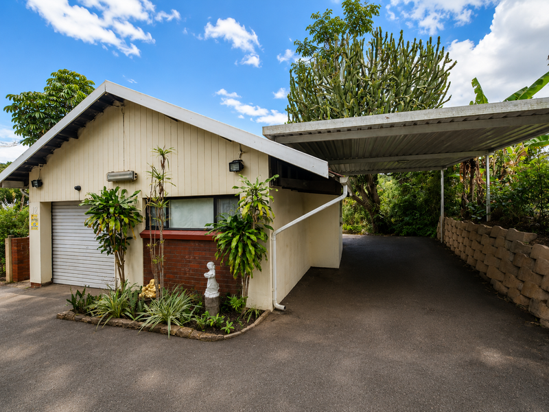 Front exterior view featuring a single garage with a roller door, an attached carport, and a brick retaining wall along the driveway.