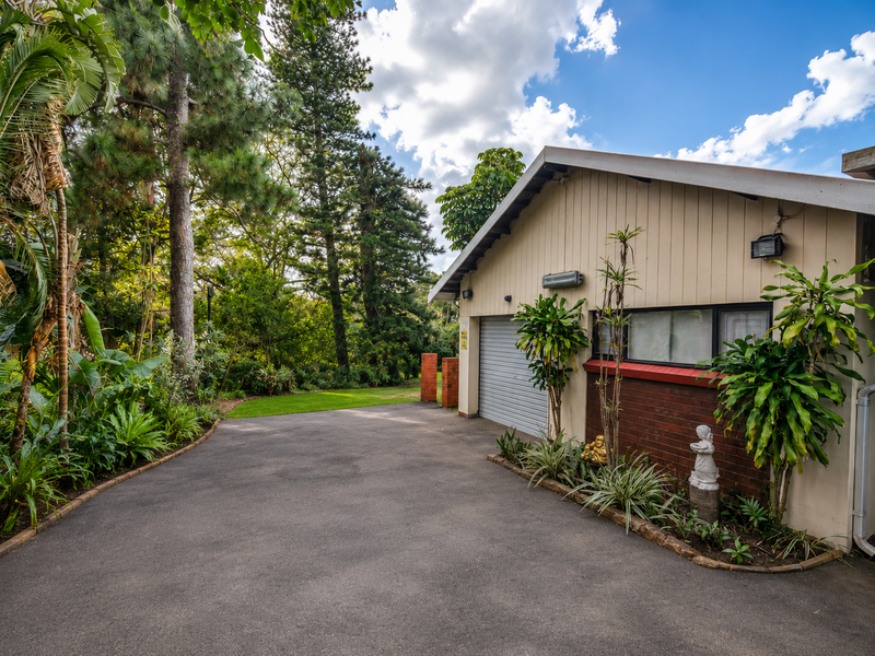 A well-maintained front exterior view featuring a garage with a brick and siding facade, set against a lush, landscaped garden and paved driveway.
