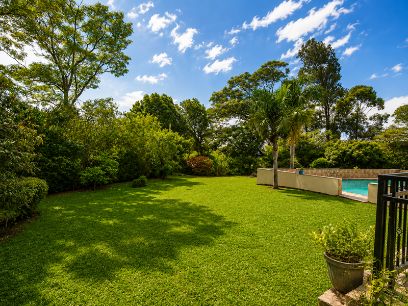 A well-maintained garden area featuring a swimming pool with a stone-clad wall and lush surrounding greenery.