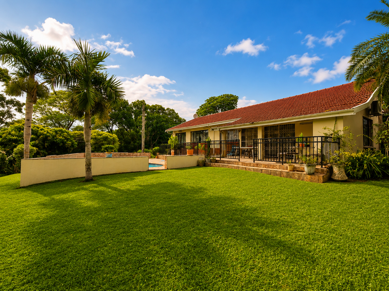 Rear view of the property featuring a spacious lawn, a covered patio area, and a swimming pool set within a well-maintained garden.