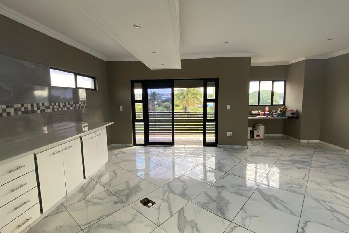 Spacious open-plan living and kitchen area featuring marble-look floor tiles, modern cabinetry, and direct access to a balcony with scenic views.