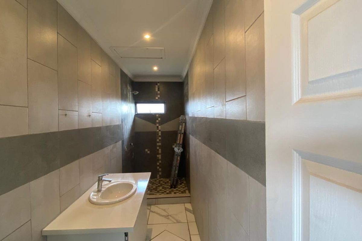 A narrow bathroom featuring tiled walls and flooring, a vanity basin, and a shower area, currently in an unfinished state.