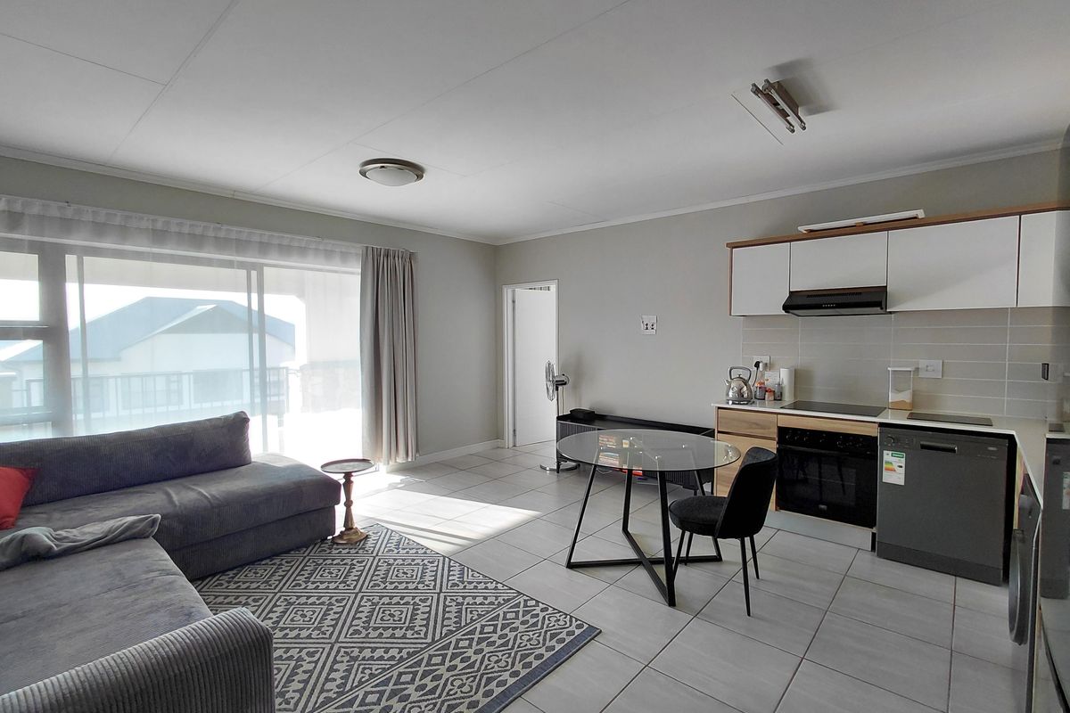An open-plan living and kitchen area featuring tiled flooring, modern cabinetry, and a sliding glass door providing access to the balcony.