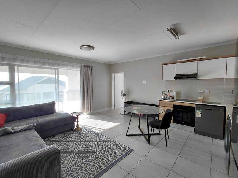 An open-plan living and kitchen area featuring tiled flooring, modern cabinetry, and a sliding glass door providing access to the balcony.