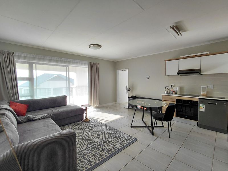 Open-plan living and kitchen area featuring tiled flooring, modern cabinetry, integrated oven, and a large sliding door providing natural light.