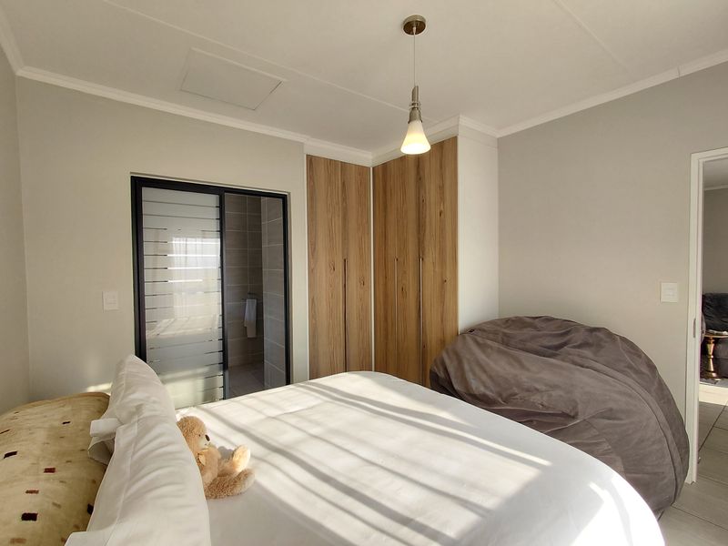 A well-maintained bedroom featuring modern wood-finish built-in cupboards, a pendant light, and a sliding door leading to an en-suite bathroom.