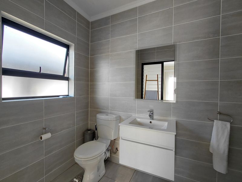 A modern, well-maintained bathroom featuring grey wall tiles, a white wall-mounted vanity with a basin, and a functional toilet.