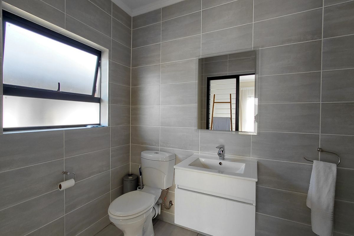 A modern, well-maintained bathroom featuring grey wall tiles, a white wall-mounted vanity with a basin, and a functional toilet.