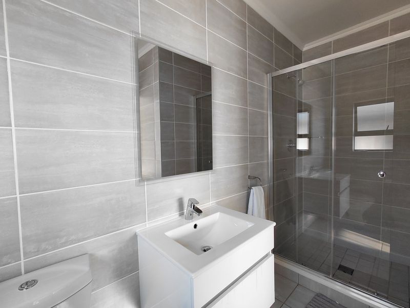 Modern bathroom featuring a sleek vanity cabinet, large wall-mounted mirror, and a spacious glass-enclosed shower with contemporary grey wall tiling.