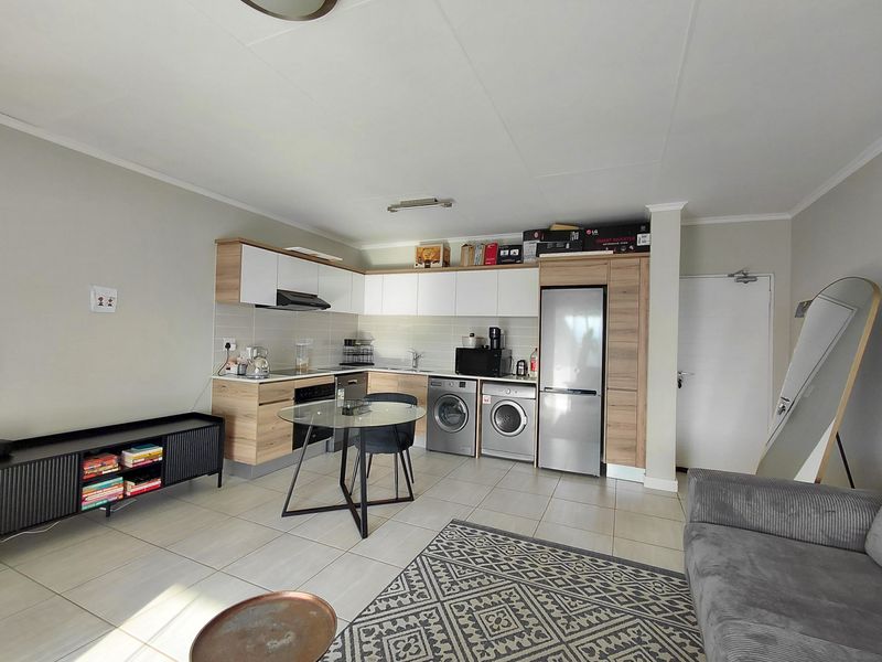 An open-plan living and kitchen area featuring modern wood-finish cabinetry, tiled flooring, and integrated kitchen appliances.