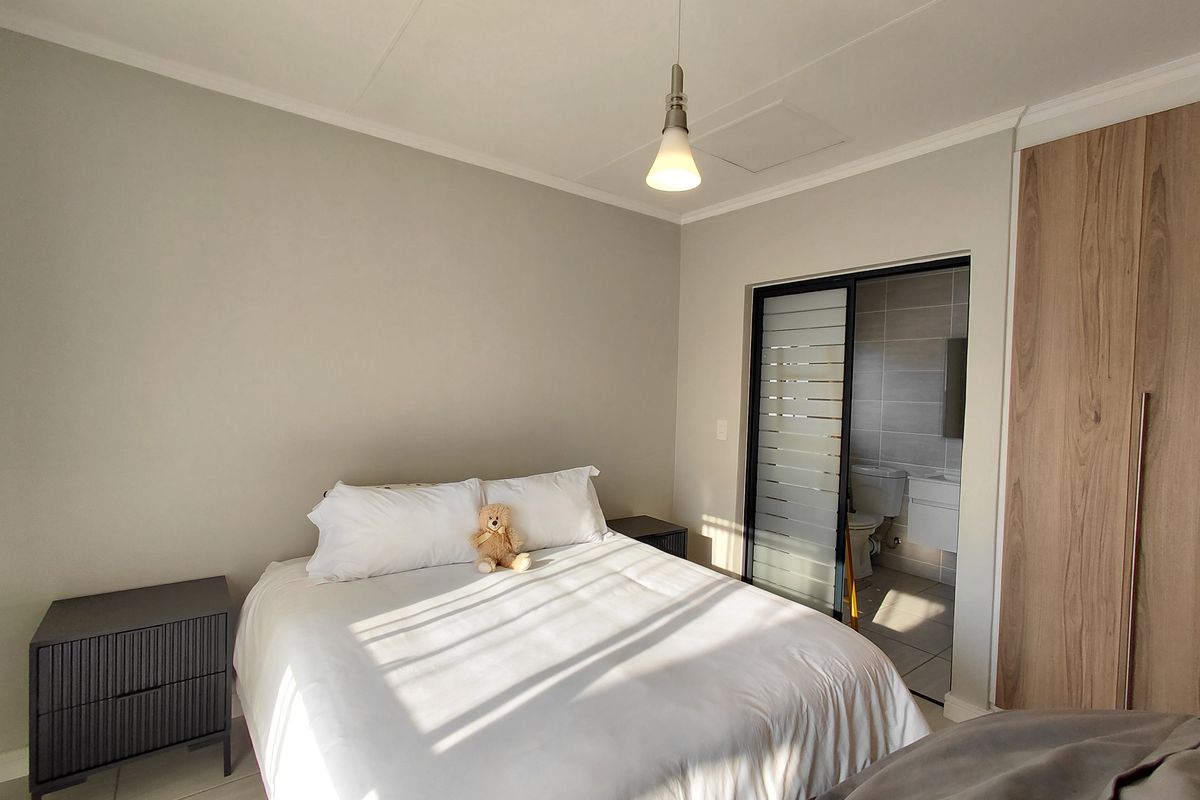 A well-maintained bedroom featuring built-in cupboards, a modern pendant light, and an en-suite bathroom accessed via a sliding door.