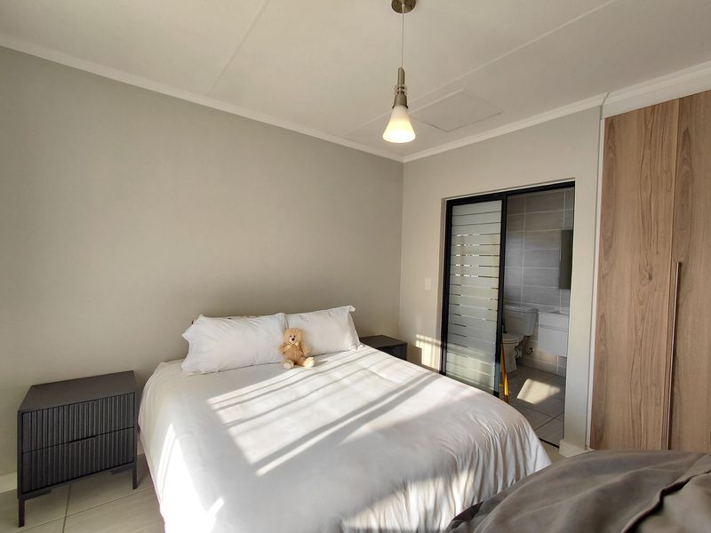 A well-maintained bedroom featuring built-in cupboards, a modern pendant light, and an en-suite bathroom accessed via a sliding door.