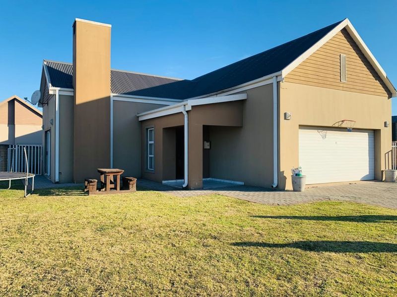 Front view of a single-story house featuring a paved driveway, attached garage, and a prominent chimney, set against a clear blue sky.