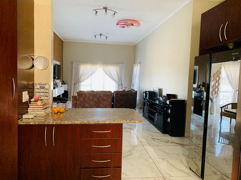 Open-plan living area featuring marble-look tiled flooring, modern kitchen cabinetry with granite countertops, and a seamless flow into the lounge space.