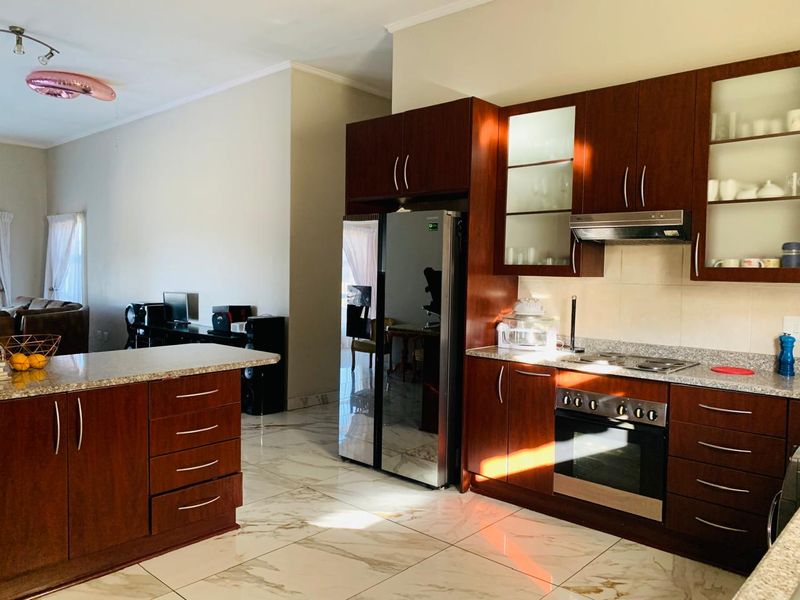 Modern open-plan kitchen featuring dark wood cabinetry, granite countertops, built-in oven, and elegant marble-look floor tiles, seamlessly flowing into the living area.