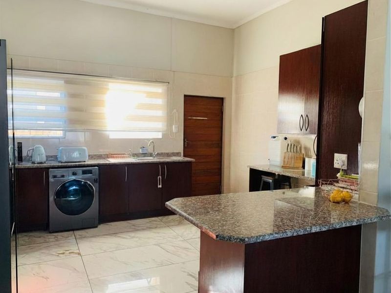 A functional kitchen featuring dark wood cabinetry, granite countertops, a breakfast bar, and tiled flooring with integrated laundry plumbing.